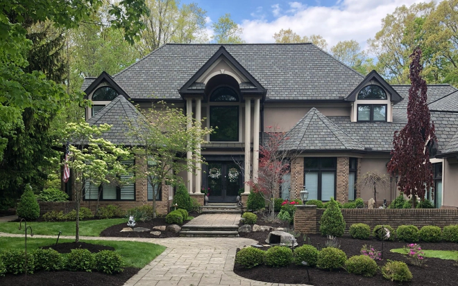 brown house with a dark grey roofing and some landscape and walkway outside